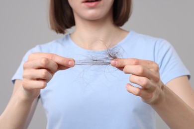 Photo of Woman holding clump of lost hair on grey background, closeup. Alopecia problem