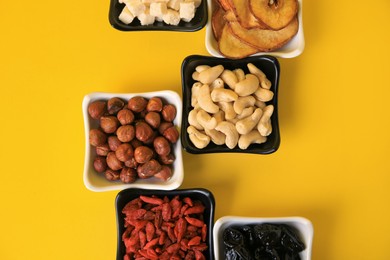 Bowls with dried fruits and nuts on yellow background, flat lay