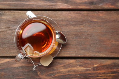 Photo of Brewing aromatic tea. Cup with teabag and spoon on wooden table, top view. Space for text