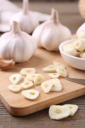 Photo of Aromatic cut garlic, cloves and bulbs on wooden table, closeup