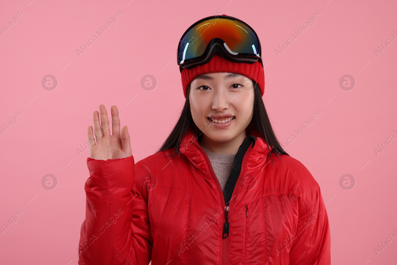 Photo of Happy woman in winter sportswear waving hello on pink background