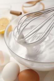 Photo of Bowl with whipped cream, whisk and ingredients on white wooden table, closeup