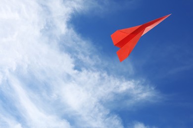 Image of Red paper plane flying in blue sky with clouds