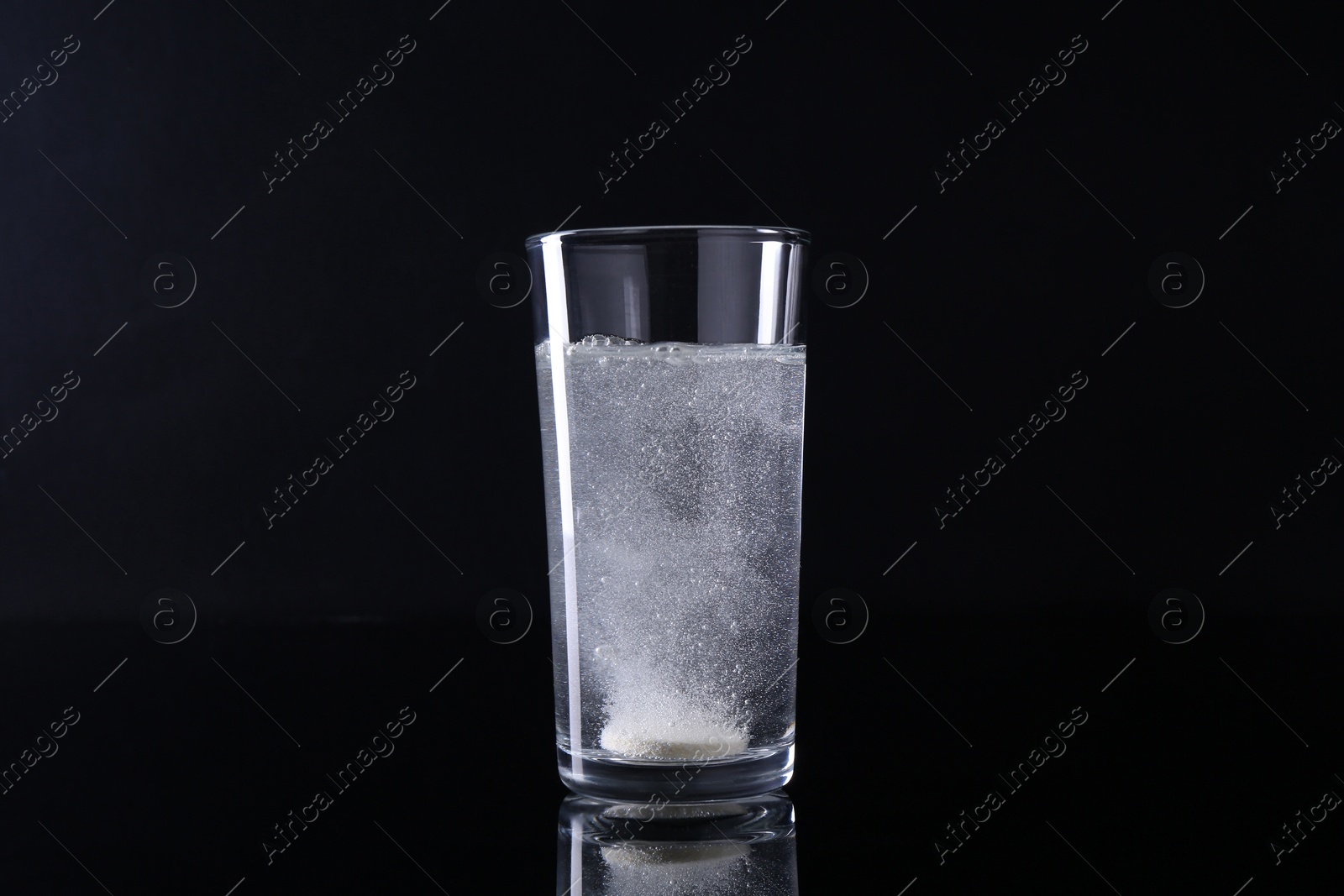 Photo of Effervescent pill dissolving in glass of water on black background