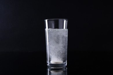 Photo of Effervescent pill dissolving in glass of water on black background