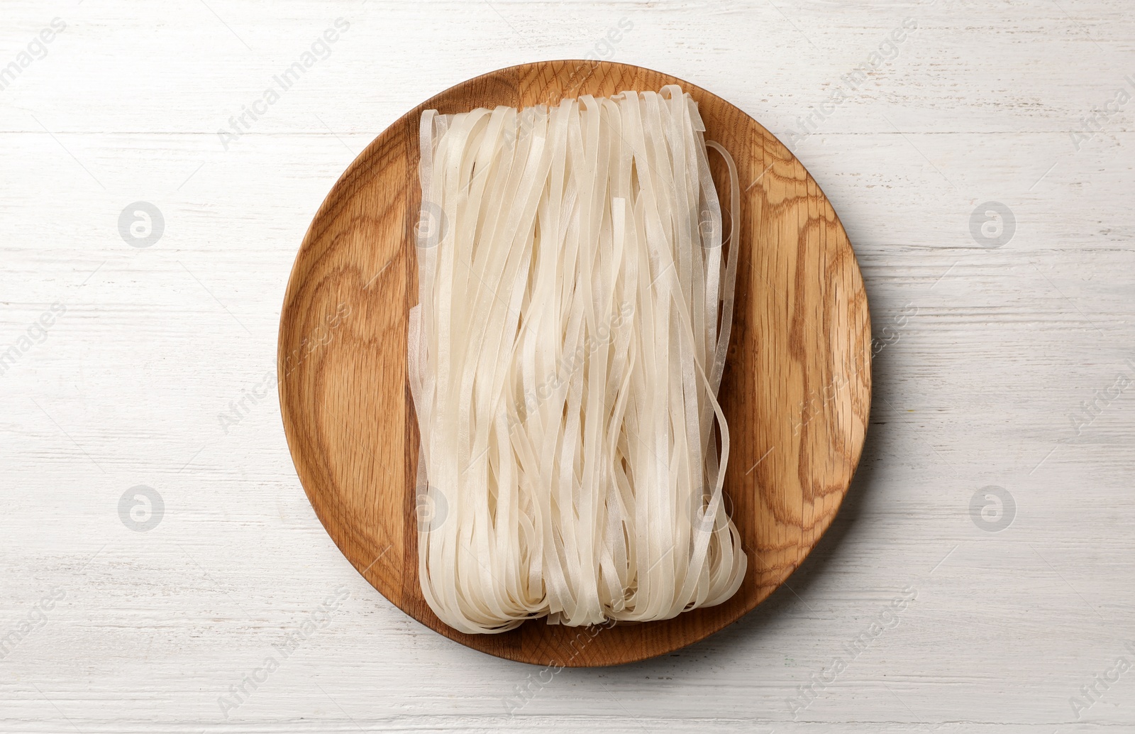 Photo of Plate with raw rice noodles on wooden background, top view