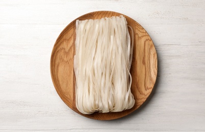 Plate with raw rice noodles on wooden background, top view