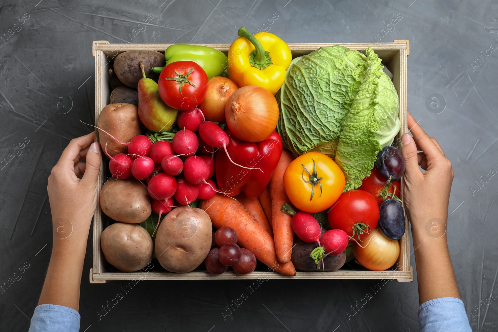 Photo of Farmer with wooden crate full of different vegetables and fruits at grey table, top view. Harvesting time