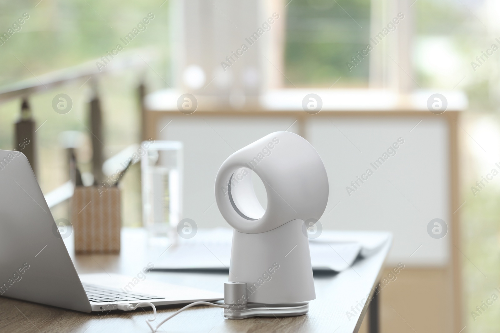 Photo of Modern portable fan on wooden table in office. Summer heat