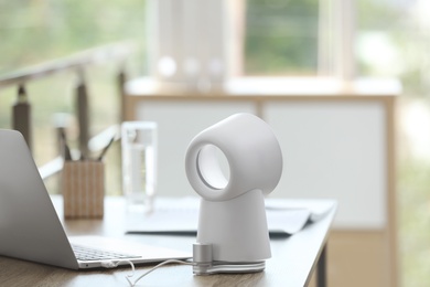 Modern portable fan on wooden table in office. Summer heat