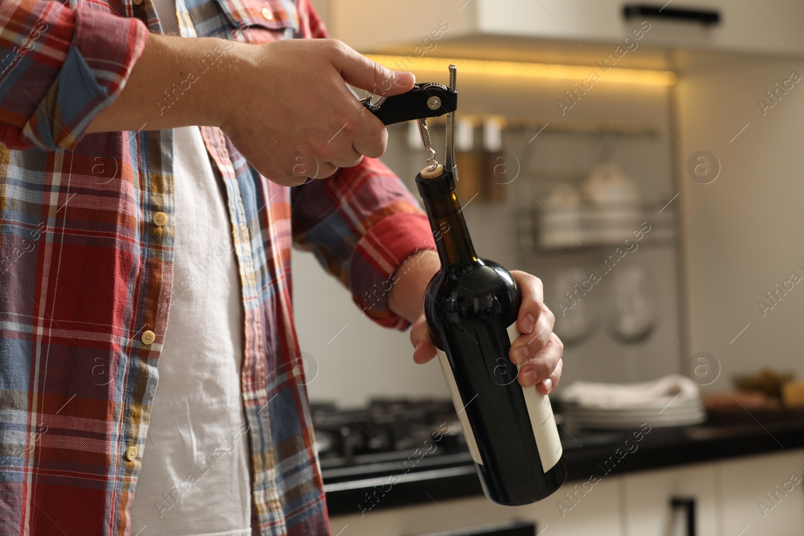 Photo of Man opening wine bottle with corkscrew indoors, closeup