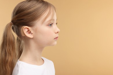 Photo of Little girl with hearing aid on pale brown background. Space for text