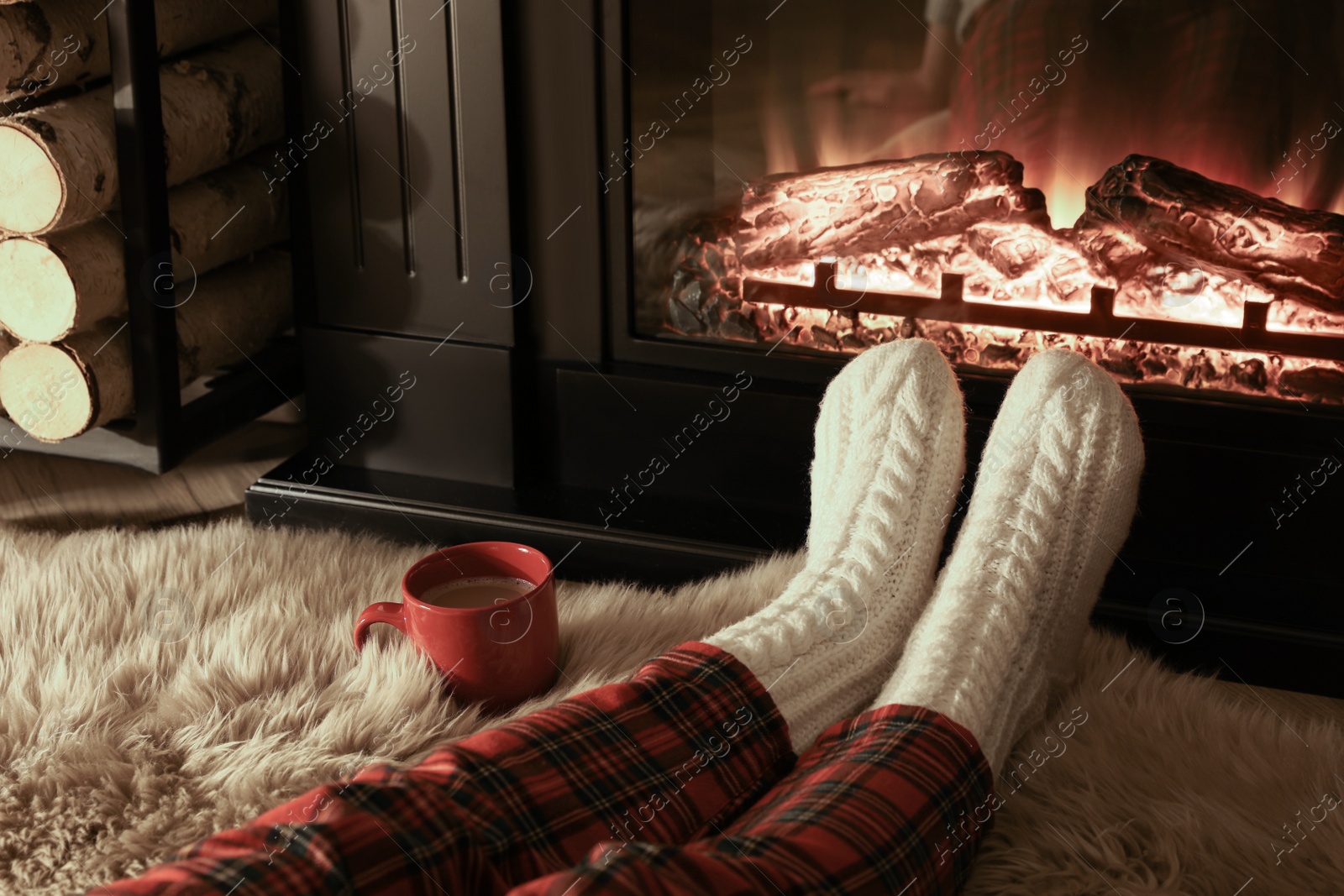 Photo of Woman in knitted socks resting near fireplace at home, closeup of legs