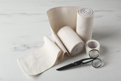 Photo of Medical bandage rolls, sticking plaster and scissors on white wooden table