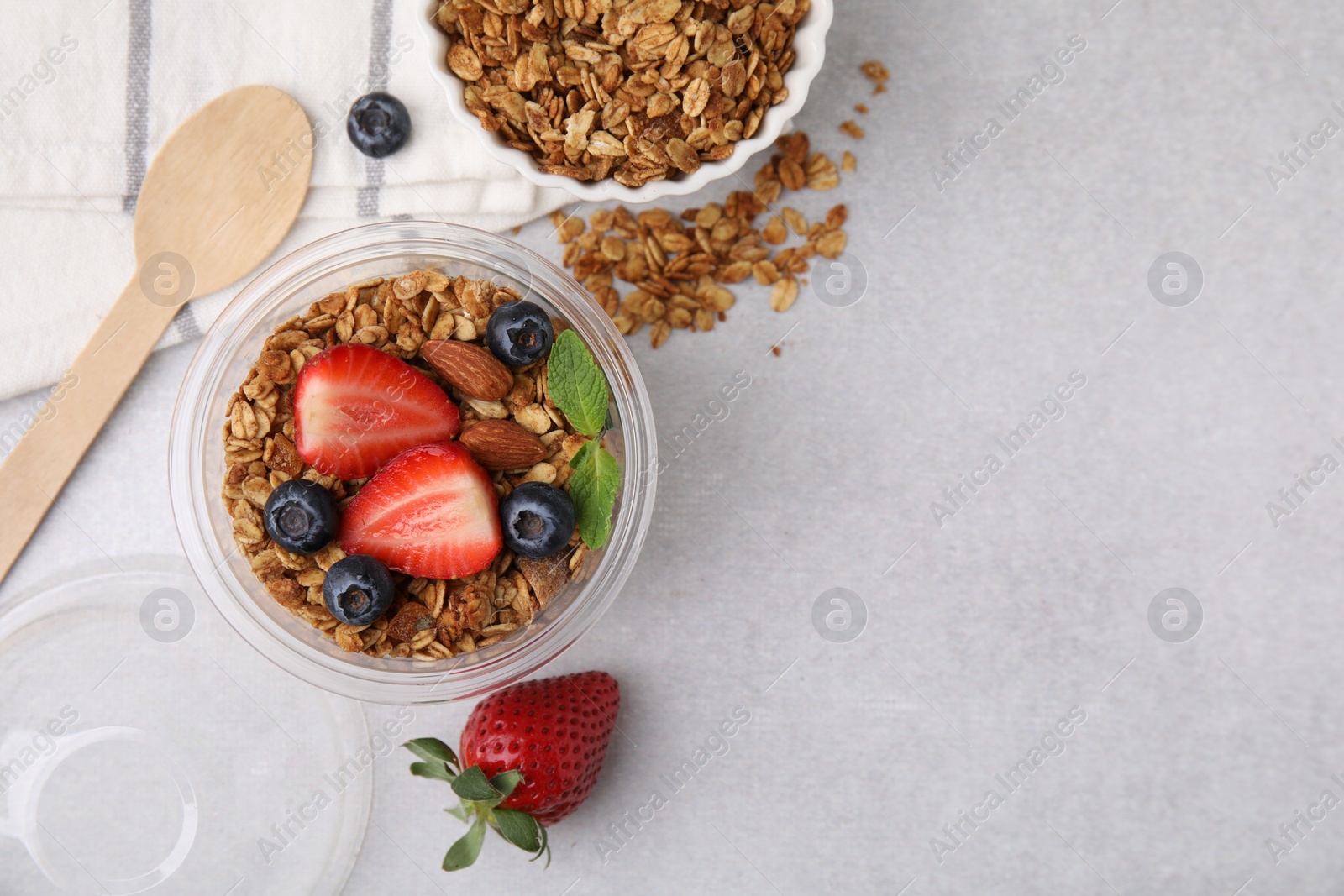 Photo of Tasty granola with berries and nuts in plastic cup on light table, top view. Space for text