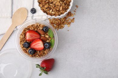 Photo of Tasty granola with berries and nuts in plastic cup on light table, top view. Space for text