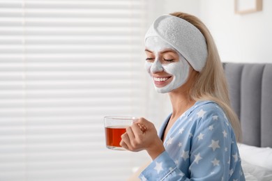 Young woman with face mask drinking tea at home, space for text. Spa treatments
