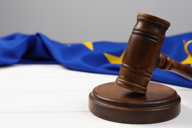 Photo of Wooden judge's gavel and flag of European Union on white table, closeup. Space for text