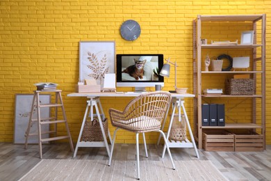 Stylish home office interior with comfortable workplace near yellow brick wall