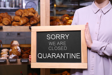Business owner holding sign with text SORRY WE ARE CLOSED QUARANTINE in bakery, closeup