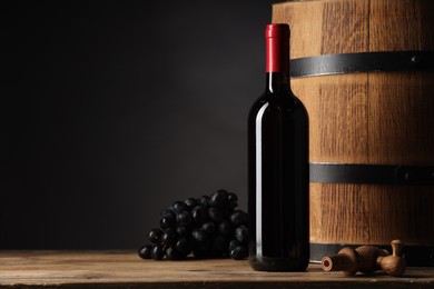 Photo of Bottle of delicious wine, wooden barrel and ripe grapes on table against black background. Space for text