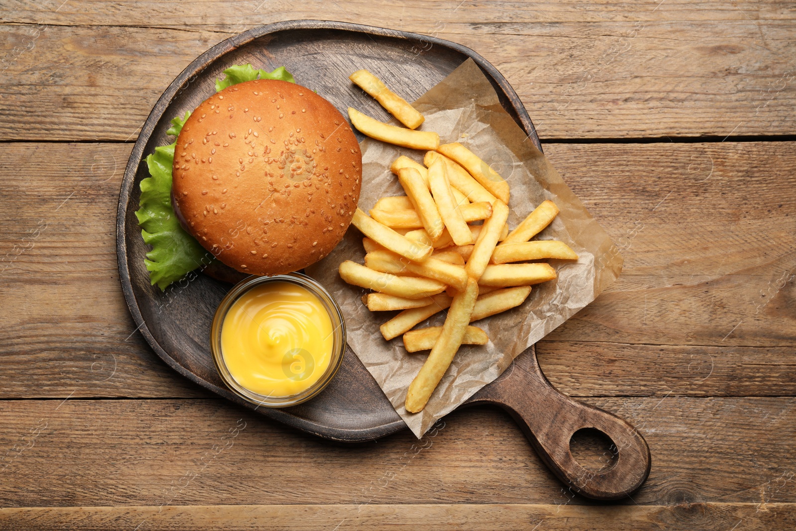 Photo of French fries, tasty burger and sauce on wooden table, top view