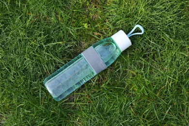 Glass bottle of fresh water on green grass outdoors, top view