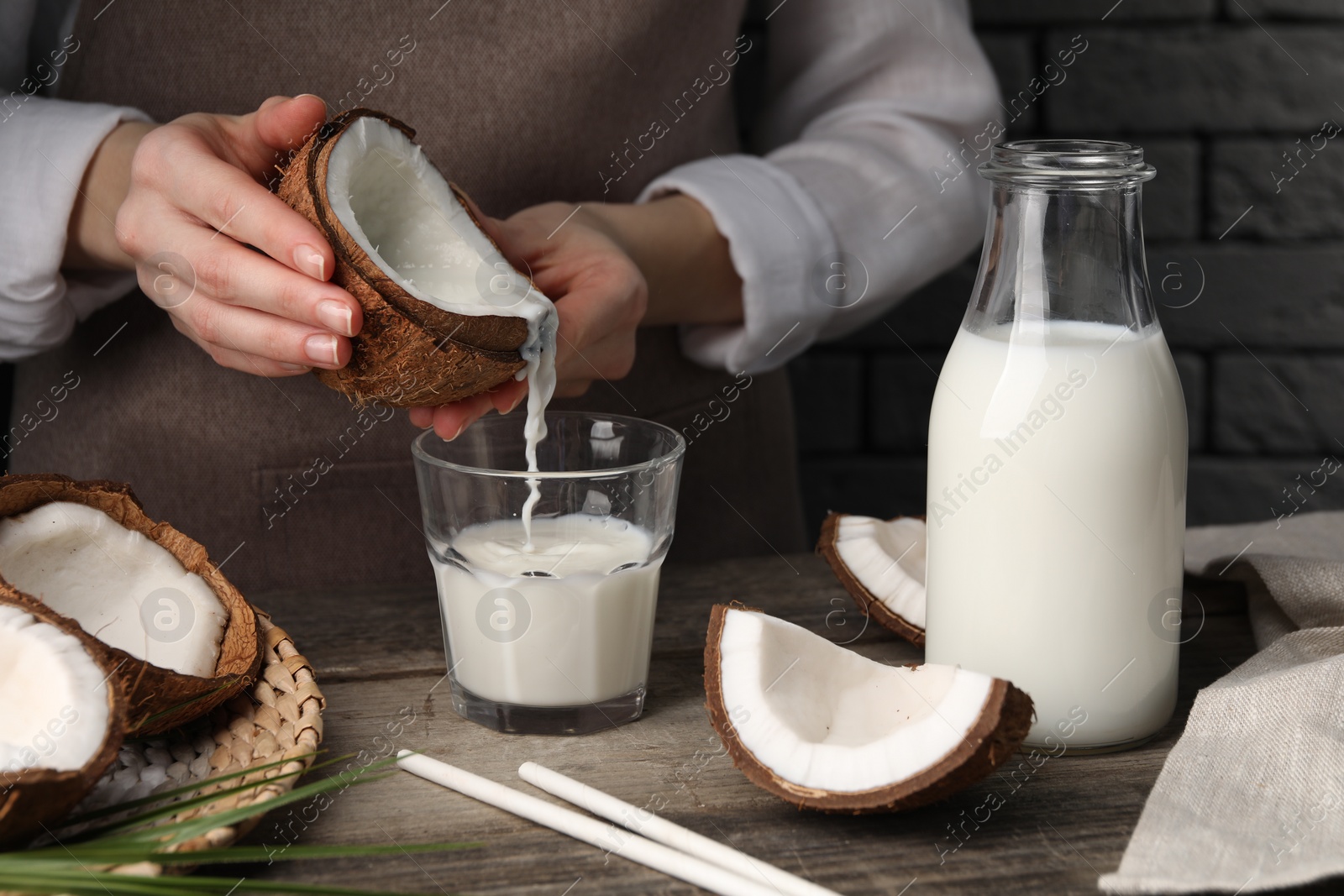 Photo of Woman pouring tasty coconut milk into glass at wooden table indoors, closeup