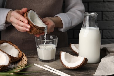 Photo of Woman pouring tasty coconut milk into glass at wooden table indoors, closeup