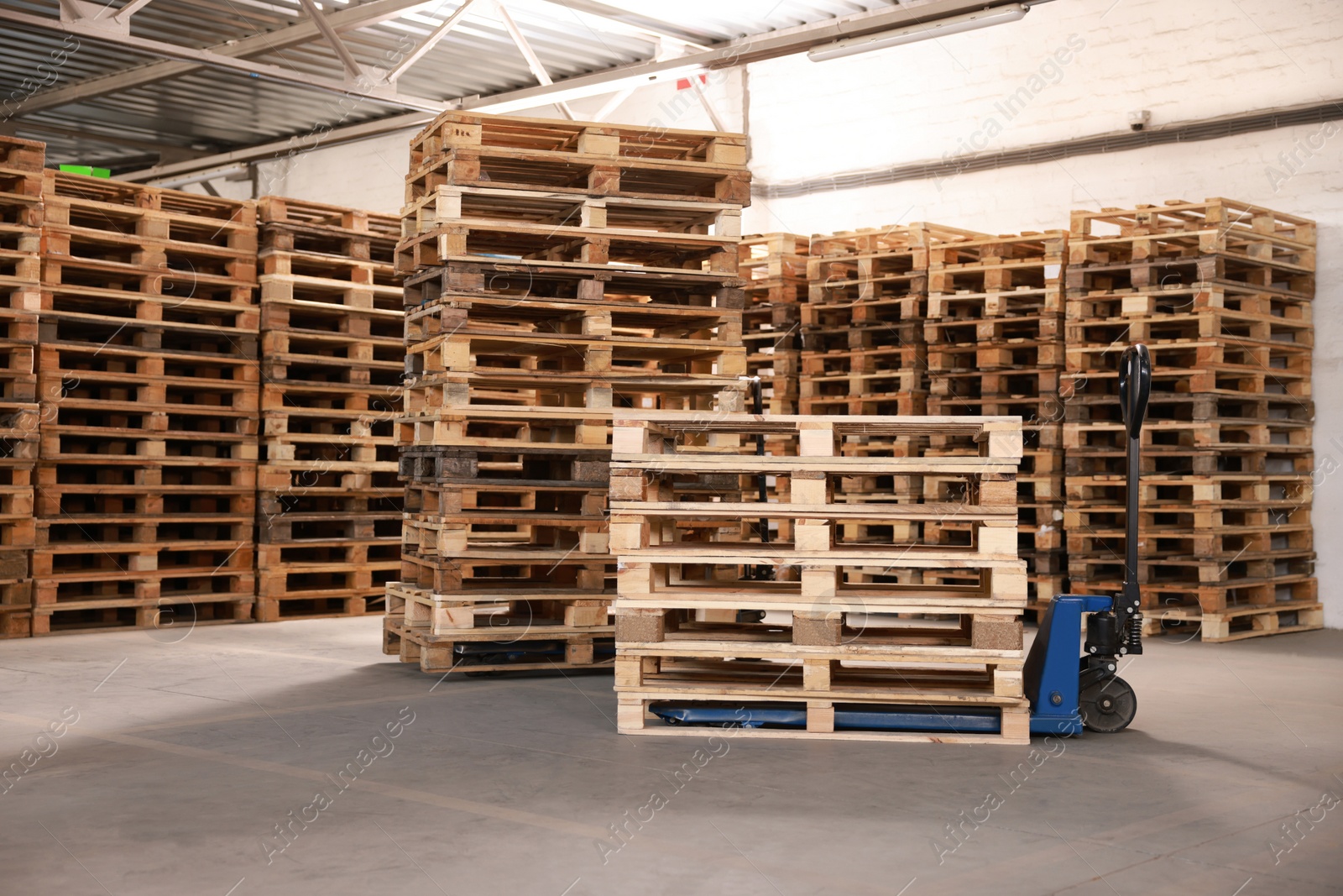 Image of Modern manual forklift and wooden pallets in warehouse