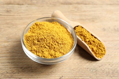 Photo of Curry powder in bowl and scoop on wooden table, closeup