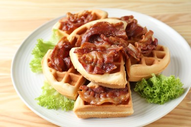 Photo of Tasty Belgian waffles served with bacon and lettuce on wooden table, closeup