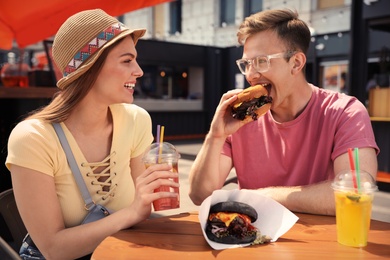 Photo of Young happy couple with burgers in street cafe