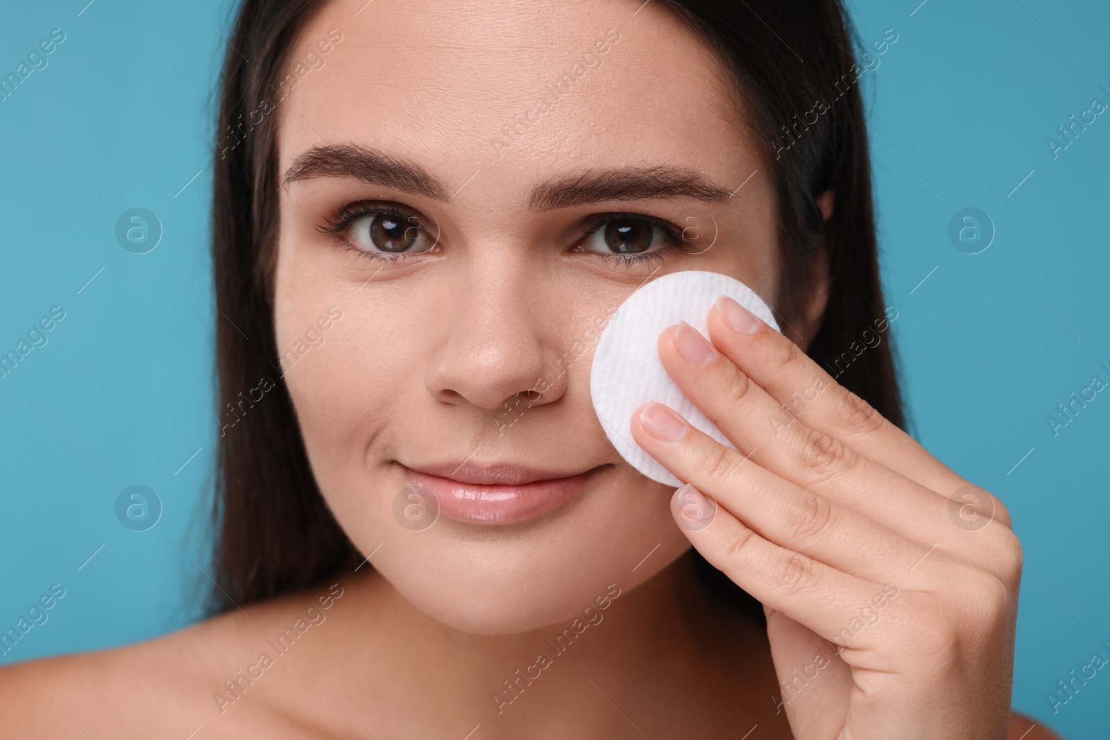 Photo of Young woman with cotton pad on light blue background, closeup