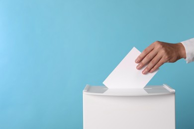 Photo of Man putting his vote into ballot box on light blue background, closeup. Space for text