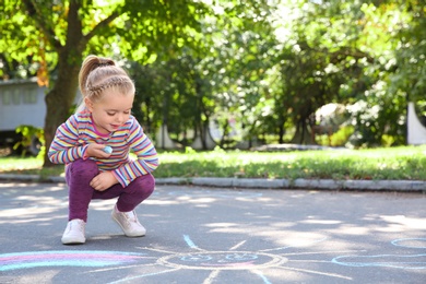 Little child drawing with colorful chalk on asphalt. Space for text