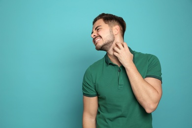Photo of Young man scratching neck on color background, space for text. Annoying itch