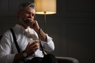 Photo of Bearded man with glass of whiskey smoking cigar in armchair indoors. Space for text