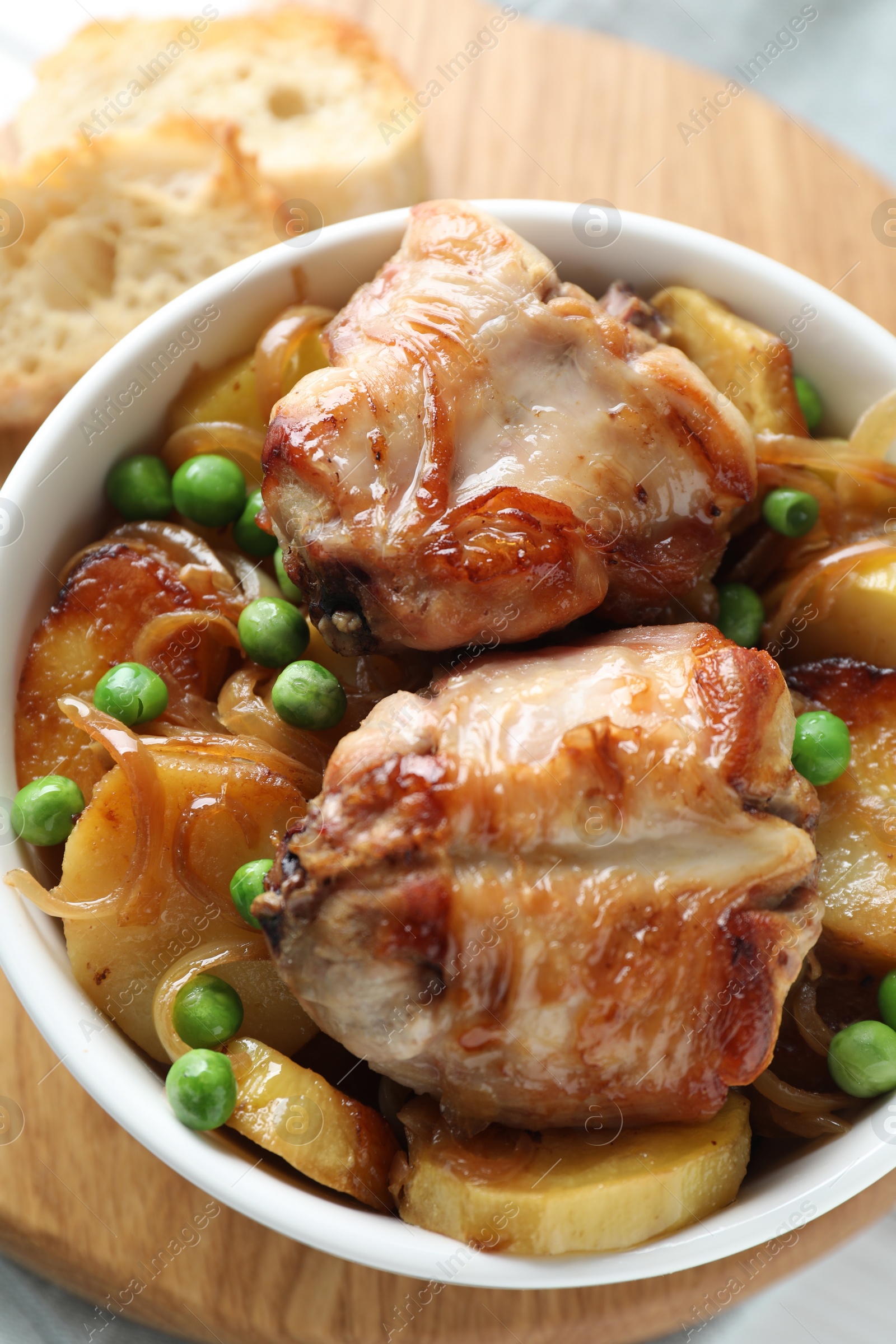 Photo of Tasty cooked rabbit with vegetables in bowl on wooden board, top view