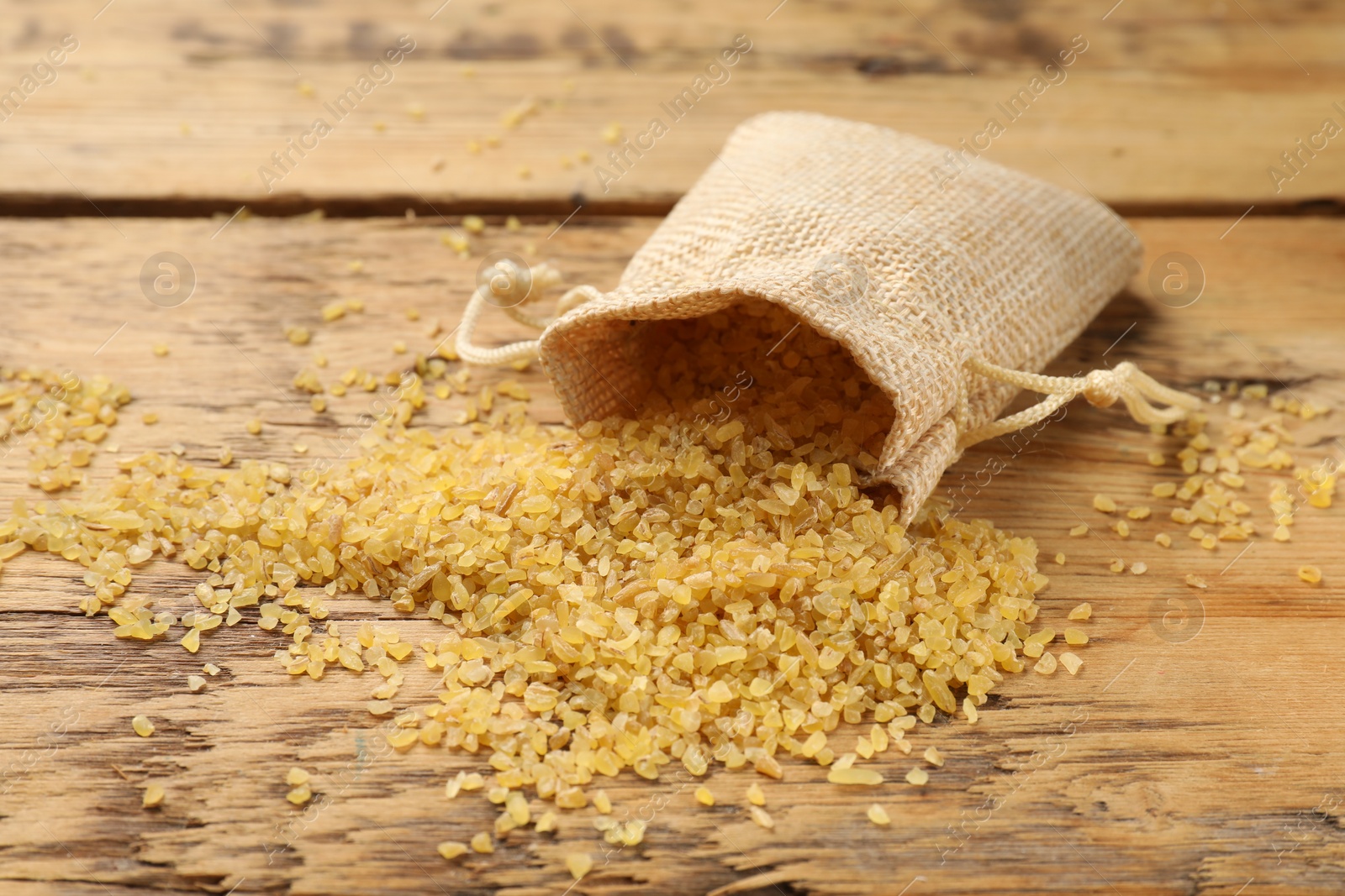 Photo of Raw bulgur and bag on wooden table, closeup