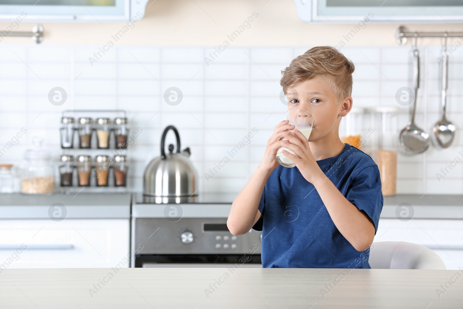 Photo of Adorable little boy with glass of milk in kitchen