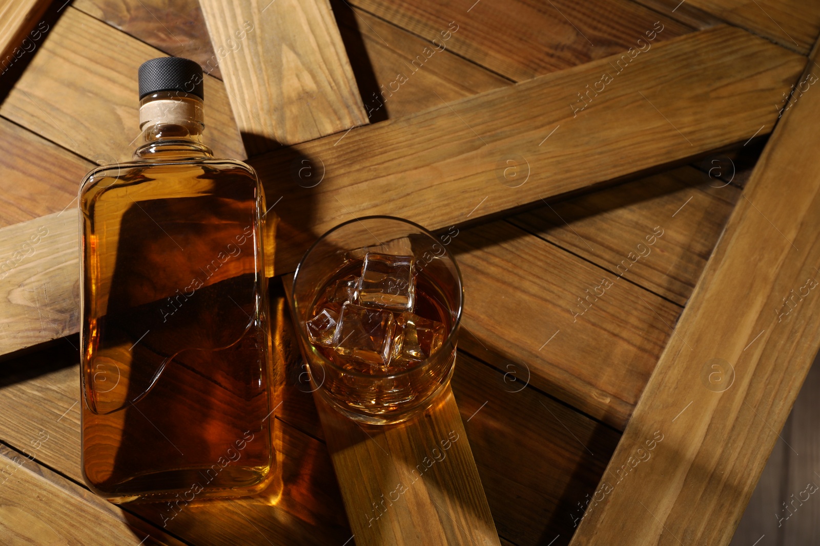 Photo of Whiskey with ice cubes in glass and bottle on wooden crate, above view. Space for text