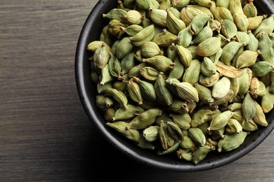 Photo of Bowl of dry cardamom pods on wooden table, top view