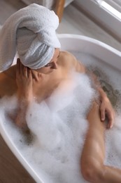 Woman taking bath in tub with foam indoors, top view