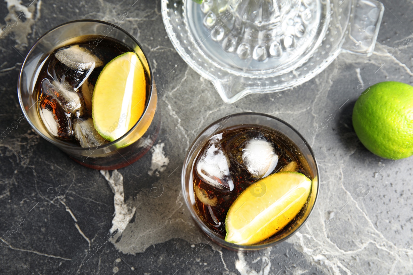 Photo of Glasses of cocktail with cola, ice and cut lime on marble background, flat lay