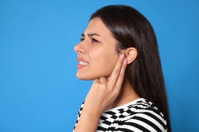 Photo of Young woman suffering from ear pain on light blue background