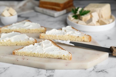 Photo of Delicious toasts with tofu cream cheese and knife on white marble table, closeup