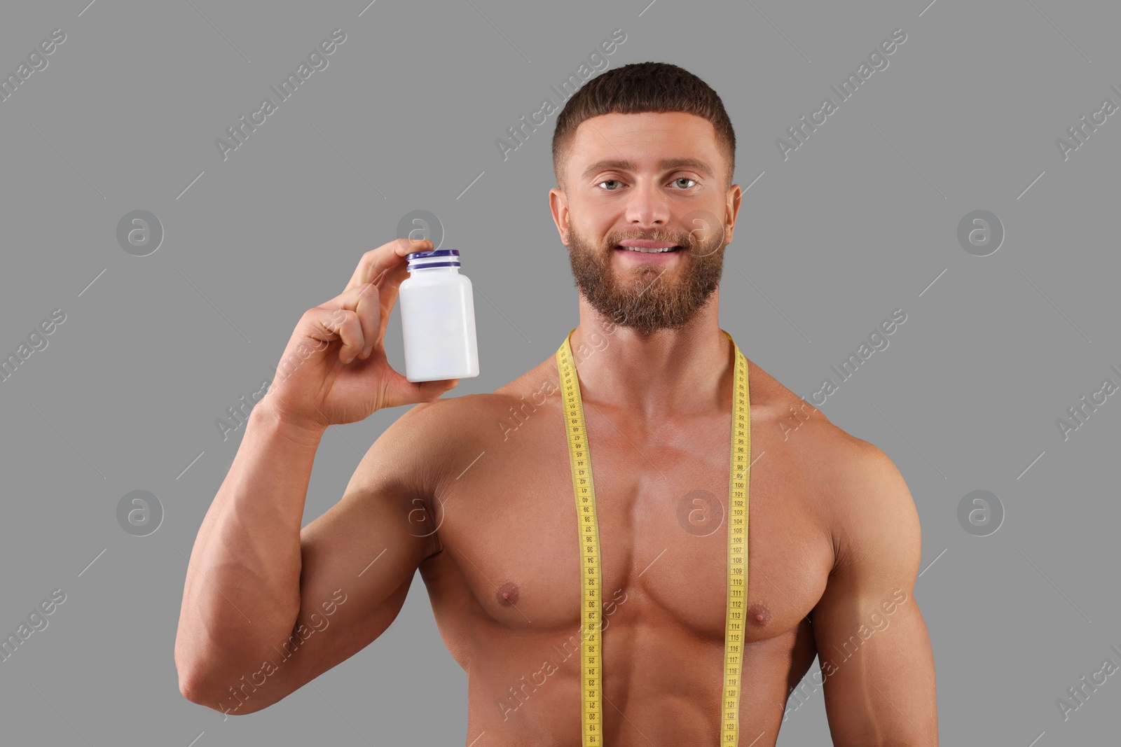 Photo of Athletic young man with measuring tape and bottle of supplements on grey background. Weight loss