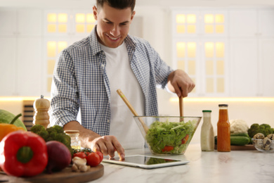 Man with tablet cooking salad at table in kitchen