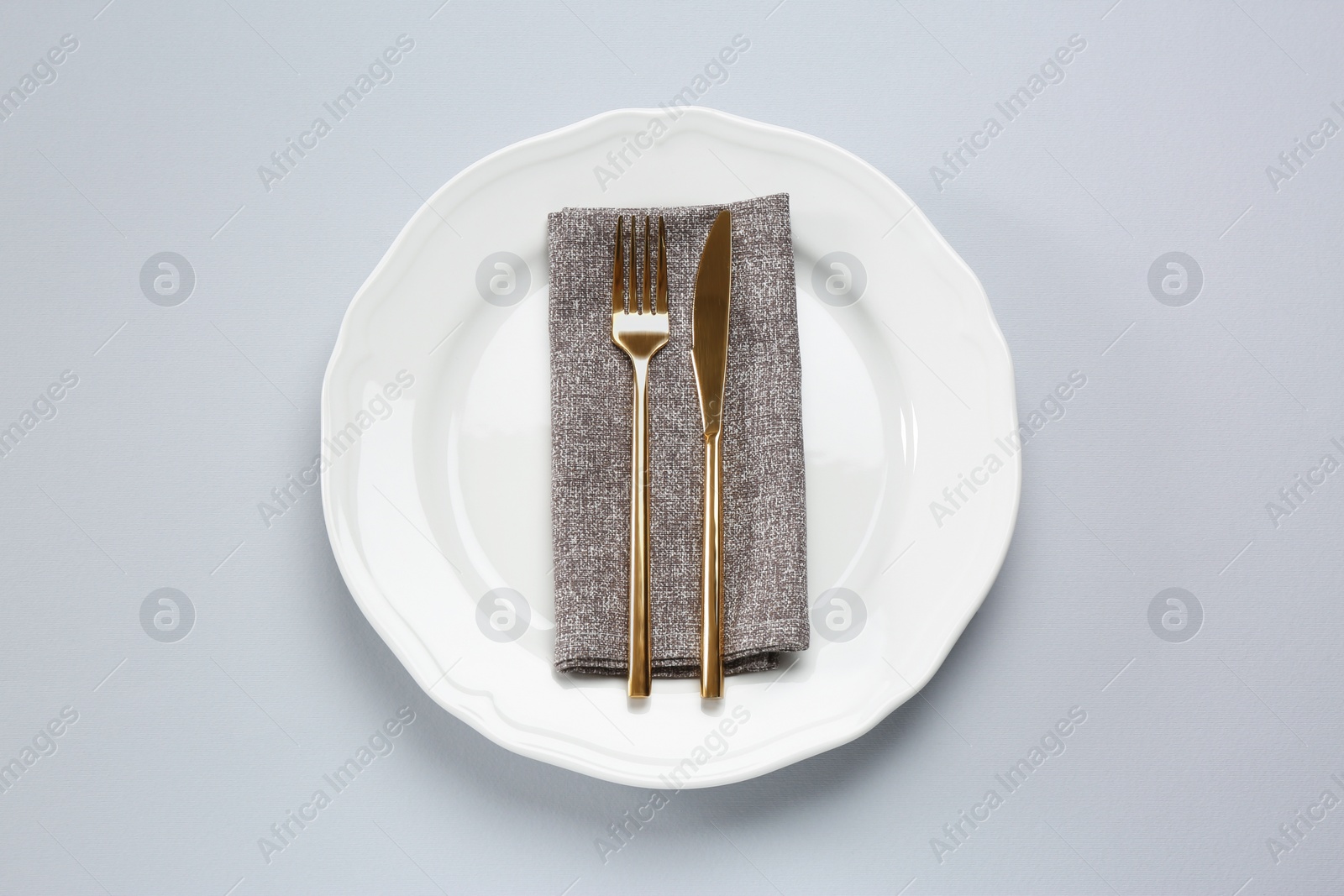 Photo of Plate, fork and knife on light grey table, top view